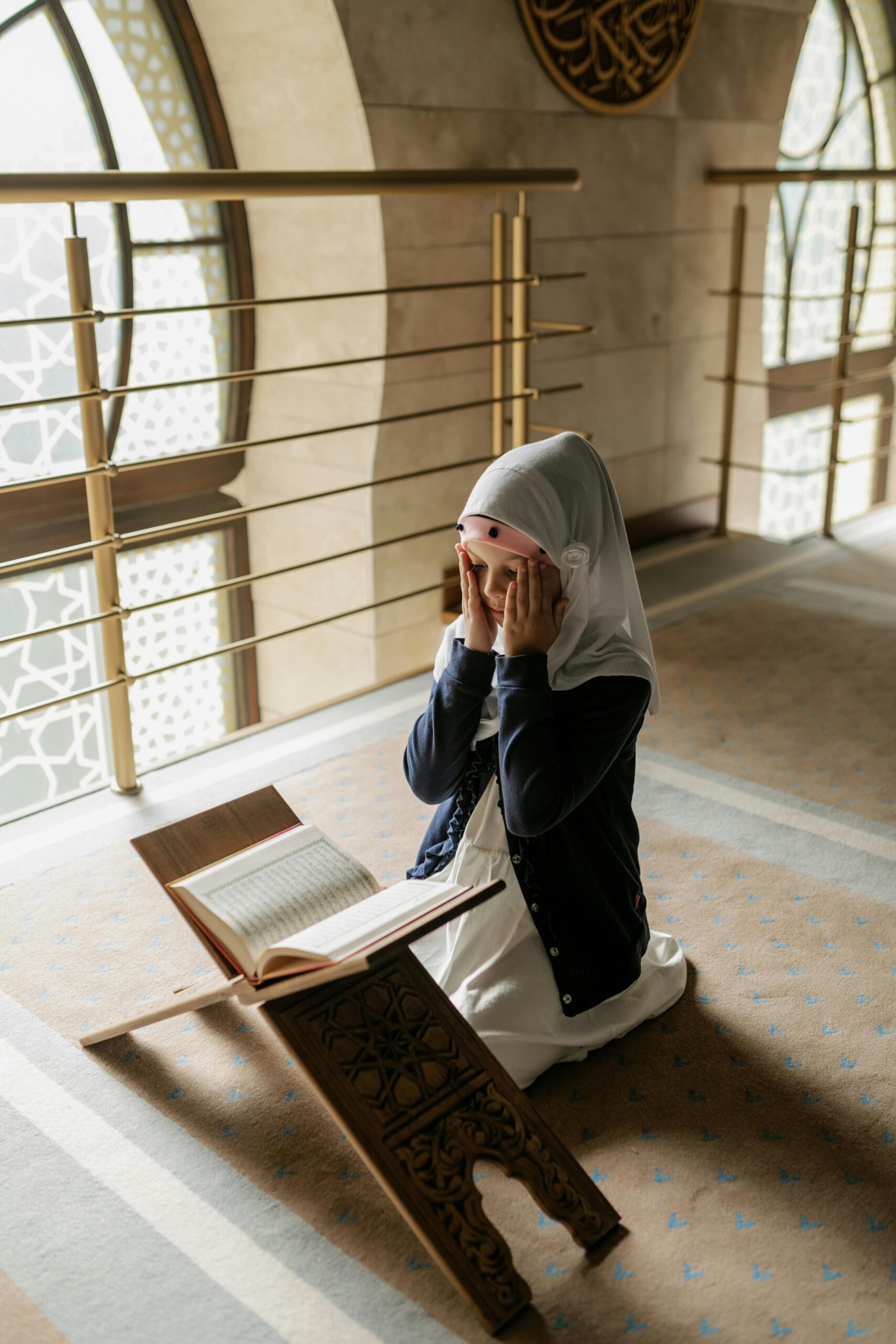 A young girl kneels and prays in a mosque, reading the Quran. Islamic culture and tradition.